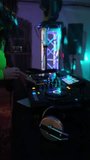 Vertical video. DJ's hands control the track on the DJ deck, people dance to music in a nightclub. Slow motion