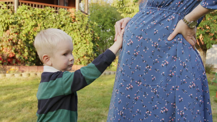 Little boy rubbing his pregnant mom's belly outdoor 