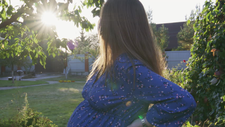 Beautiful pregnant woman enjoying fresh air at sunset rays on the backyard