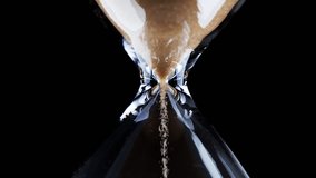 Hourglass. Sands move through hour glass. Sandglass close-up on a black background. Slow motion video. A pile of Golden sand at the bottom of the hourglass, small grains of sand fall from above.