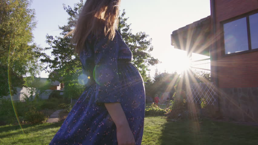 Beautiful pregnant woman enjoying fresh air at sunset rays on the backyard