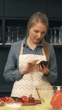 Young woman uses smartphone while cooking in the kitchen. Vertical video