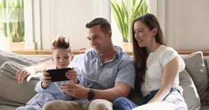 Beautiful family with little son spend time in living room, sit on couch using modern smart phone, play new cool popular videogame, watching online videos, enjoy mobile application on weekend at home