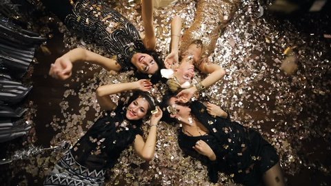 Young women in glitter dress lying on the floor and enjoying confetti on the new year party. Super slow motion.