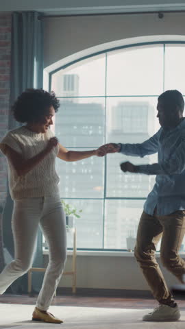 Cinematic Vertical Shot of Excited Young Couple in Love Run Into the Frame and Started Dancing in the Middle of the Living Room. Bright Modern Home with Happy Young People. Slow Motion