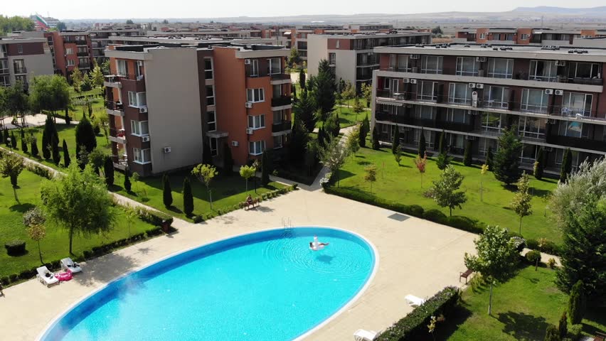 Beautiful woman on unicorn pool float in pool in fron of hotel from above view. Summer holidays. Aerial top view from drone