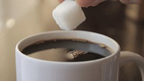 Slow Motion Hand Dropping Sugar Cube Into Black Coffee. Sugar Falling Down Into Coffee Cup. Coffee Caffeine Addiction Junk Food. Concept of Unhealthy Eating, Diabetes, Obesity, Heart Disease.  - Powered by Shutterstock - Get 15% off with code: PIKWIZARD15