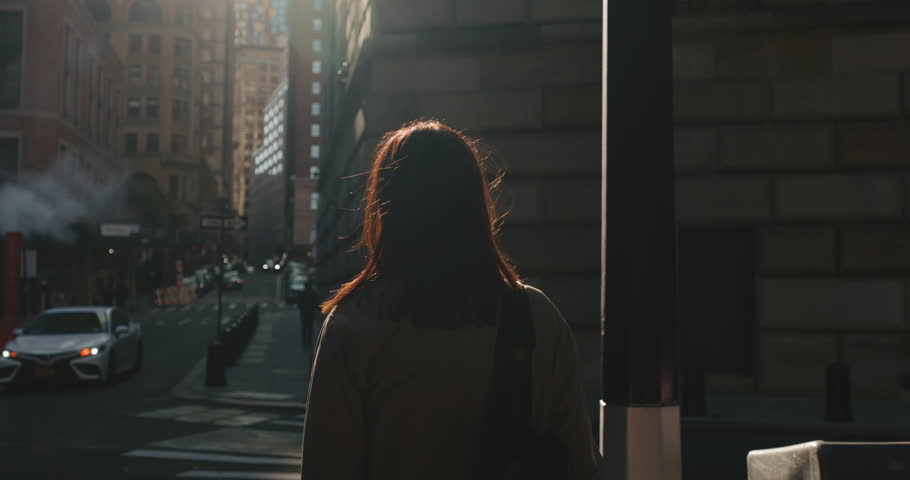 Woman standing at the crosswalk and looks around in cinematic urban New York City street.