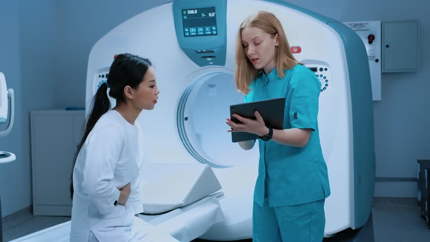 Patient complaining of stomach ache to her doctor while seating on scanning table, X-ray inspection of biopsy at contemporary clinic. MRI machine and contemporary equipment in medical facility. Royalty-Free Stock Footage #3452424451