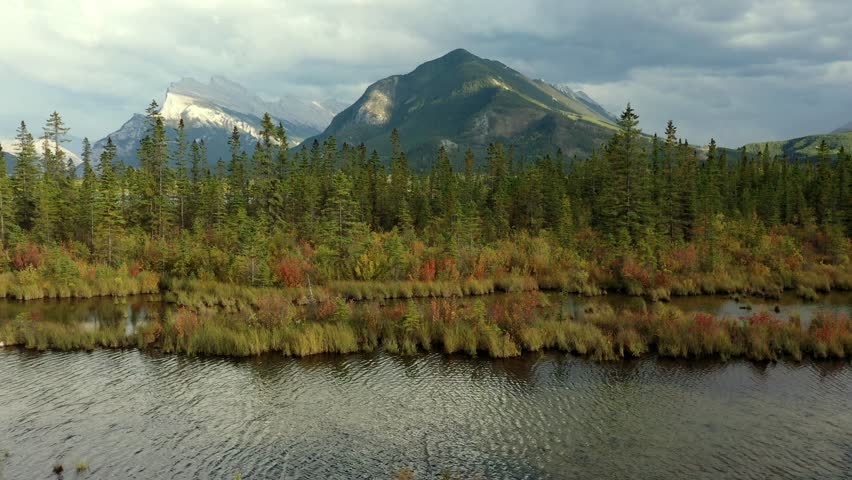 Beautiful aerial view of the Vermilion Lakes and Sulphur Mountain full of pine trees, in autumn on a cloudy day near Banff, Canada. Royalty-Free Stock Footage #3452430451