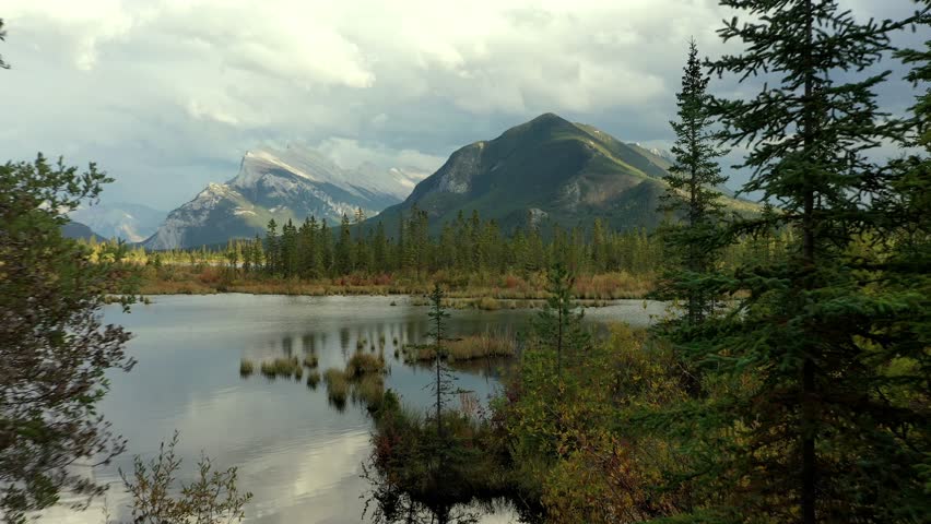 Beautiful aerial view of the Vermilion Lakes and Sulphur Mountain full of pine trees, in autumn on a cloudy day near Banff, Canada. Royalty-Free Stock Footage #3452430939
