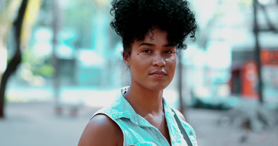 One happy young black Brazilian woman smiling at camera, tracking shot close-up face of a South American female 20s person with curly hair of African descent with friendly expression