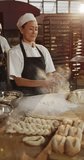 Vertical video of portrait of happy asian female baker preparing dough in bakery. global business and bakery.