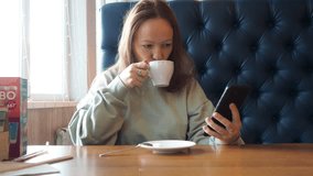 women's hands holding cell telephone, girl watching video on mobile phone during coffee break. a woman sits in a cafe, communicates on the Internet, takes a selfie, call online, text messages.