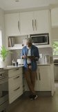 Vertical video of happy senior african american man drinking coffee and using tablet. healthy, active retirement at home.