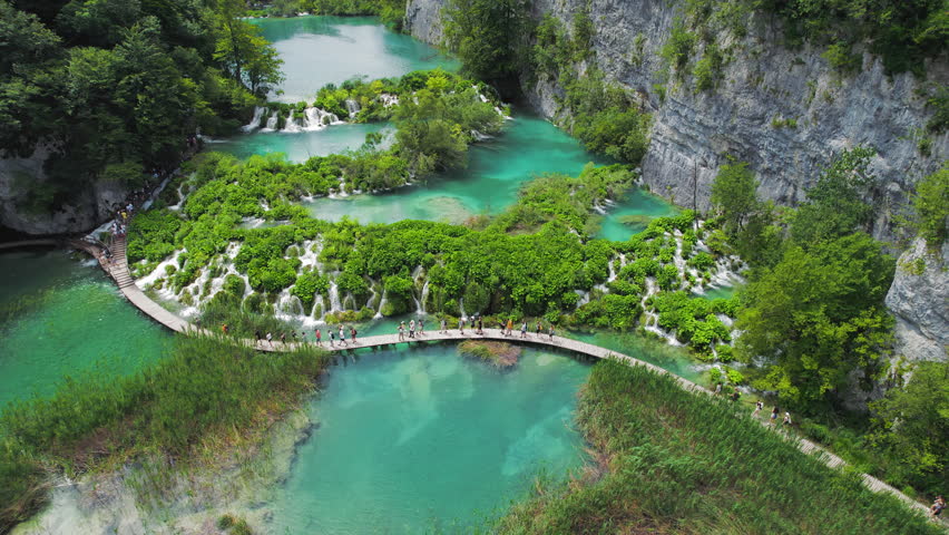 Hiking trail over crystal clear emerald water of lake. Path for tourists in mountain national park with waterfalls. Plitvice Croatia.