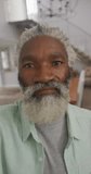Vertical video of portrait of happy senior african american man talking at home. healthy, active retirement at home.
