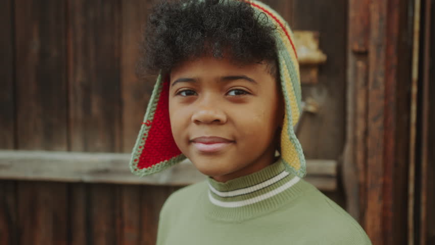 Little African-American boy smiling and posing for camera against wooden wall in the garden. Video portrait