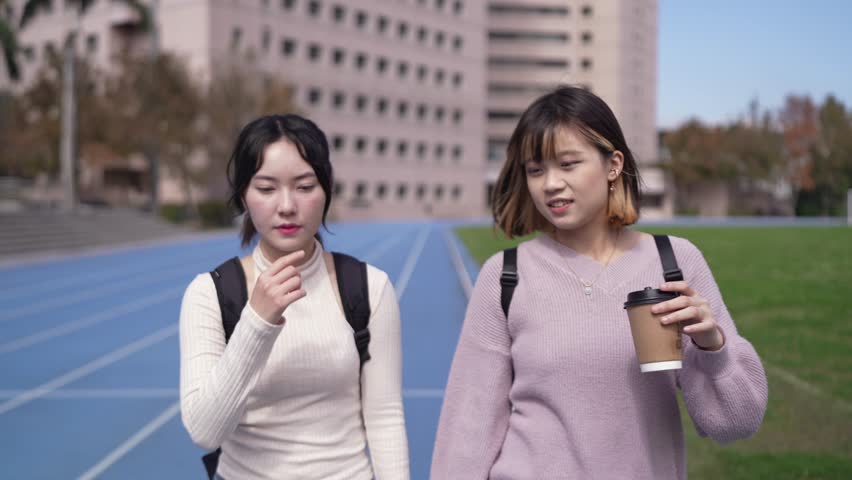 Two Taiwanese female college students in their 20s walking while talking about university campuses in Taipei City, Taiwan