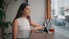 Friendly girl wearing earphones for remote meeting at cafe window closeup. Smiling thai woman greeting to web camera laptop starting video call. Happy beautiful female student joining to online lesson