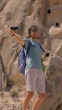 Vertical video. Young man tourist explores the extraordinary rock formations that tell the ancient tales of Cappadocia, Turkey. These surreal rocks, once homes carved by ancient inhabitants, stand as