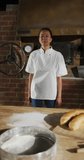 Vertical video of portrait of happy asian female baker in bakery. global business and bakery.