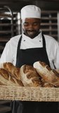 Vertical video of portrait of happy african american male baker with bread in bakery. global business and bakery.