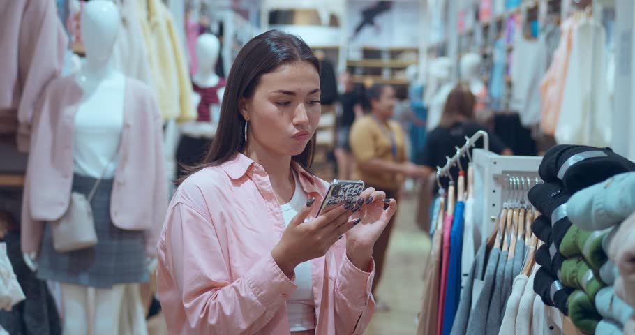 Woman standing in store consulting friend via phone about clothing choice. Clothing choice reflects happiness friendship Clothing choice aided by technology symbol modern lifestyle. Royalty-Free Stock Footage #3452765837