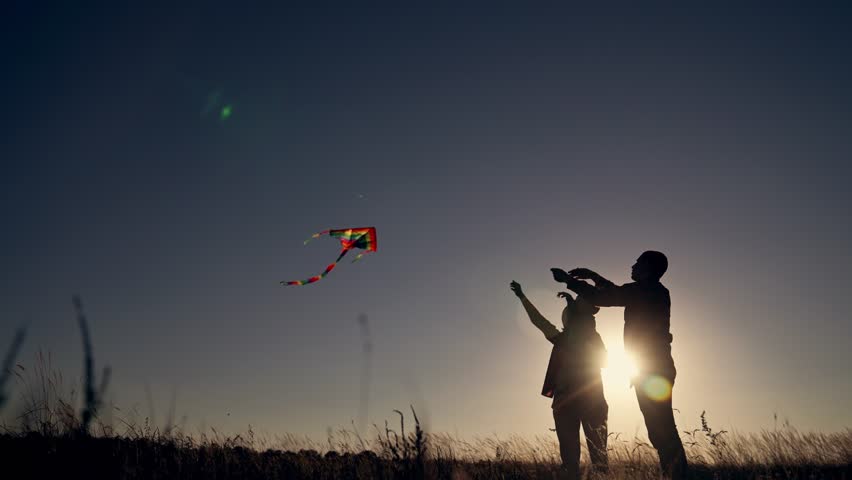Happy family. People in park launch flying kite. Family in grass at sunset are playing together. Son, daughter and parents launch kite in wind. Happy family concept. Kite soars in the wind in the sky