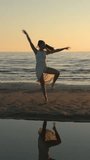 Young woman in white dress dancing on beach at evening time. Vertical video