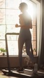 Vertical Video. Beautiful Athletic Sports Woman Running on a Treadmill at Her Home Gym. Energetic Workout Athlete Training while Listening Podcast or Music in Headphones. Apartment with Window View
