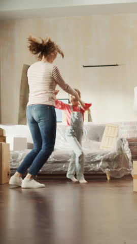 Vertical Screen: Happy Mother and Daughter Moving Into their New Cozy Home. Cheerful Young Family, Girls Have Fun, Dance, Hug in the Middle of Apartment. Living Room Has Unpacked Cardboard Boxes Royalty-Free Stock Footage #3452875019