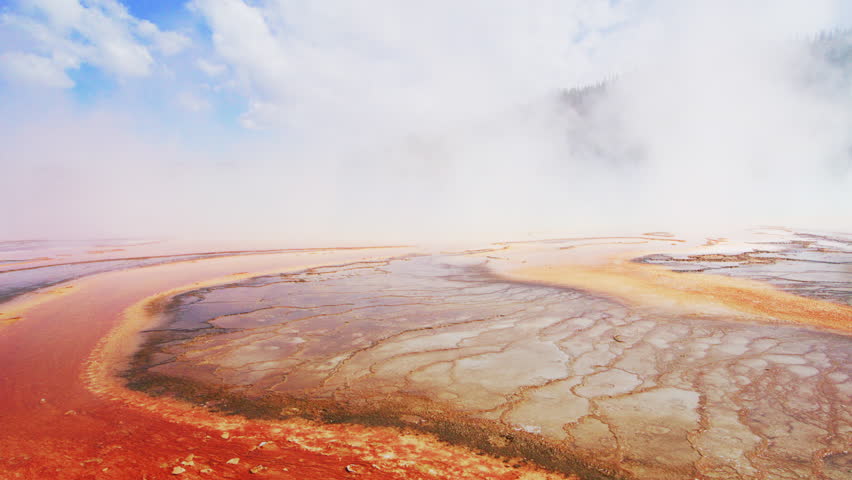 Hazy sky over a vast sulfuric geyser basin with intricate mineral patterns and geothermal activity. Earth