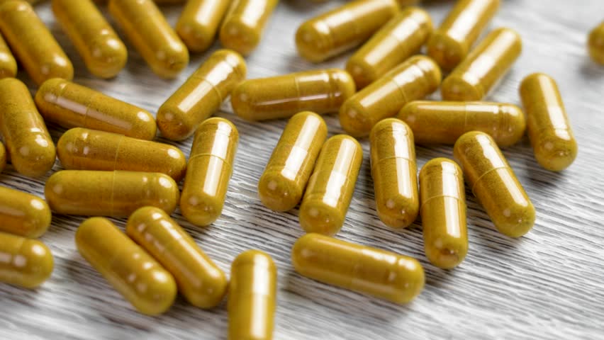 Turmeric supplement capsules on a board close up. Herbal natural medicine pills with curcumin powder. Rotation