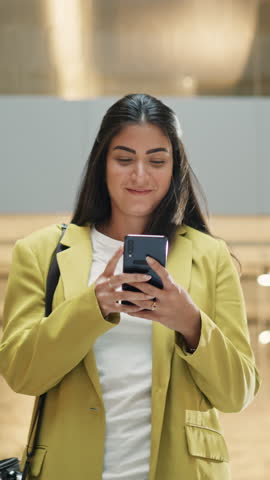 Vertical Shot: Portrait of a Latin Woman Looking at her Smartphone and Walking in a Corporate Office Building. Businesswoman Smiling as She Receives a Salary Raise. Tracking Slow Motion Royalty-Free Stock Footage #3453022155