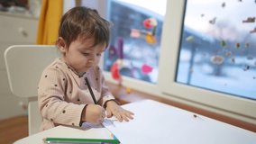 baby girl draws while sitting at table by the window at home. happy family kid concept. baby daughter learns to draw with pencils on dream a sheet of paper indoors. development of fine motor skills - Powered by Shutterstock - Get 15% off with code: PIKWIZARD15