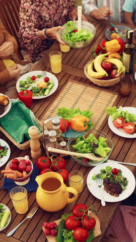 Vertical Screen: Top Down Elevated View at a Family and Friends Celebrating Outside at Home. Children, Adults and Seniors Sitting at a Table, Having Fun Conversations. Eating Barbecue and Vegetables.