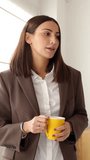 Vertical video of young business woman talking in the office. Businesswoman having a coffee break with colleague at workplace. Teamwork and business concept