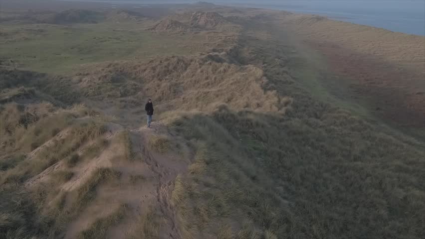 Sunrise scene. Wanderer above the sea of fog. Epic Drone video of a person standing on top of a sand dune at sunrise looking out to sea over the fog. Moody, Tranquil 