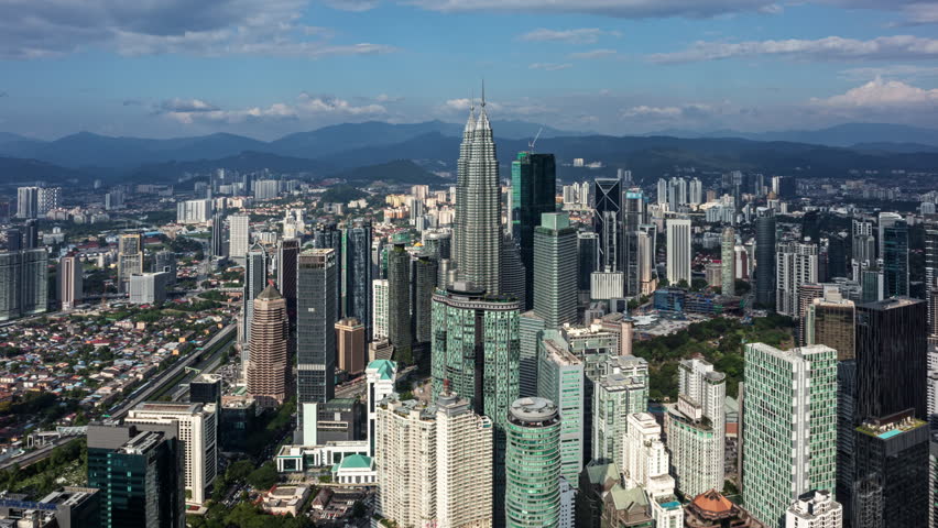 sprawling urban landscape of Kuala Lumpur, showcasing towering skyscrapers amidst the verdant hills under a clear sky