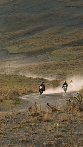 In this dynamic snapshot, three motorcyclists race down a remote dirt road, their presence marked by plumes of dust trailing behind them. Against a backdrop of rolling hills, they tackle the uneven Royalty-Free Stock Footage #3453290003