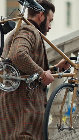 Young stylish man carrying his bicycle upstairs, retro bike in sunny day.