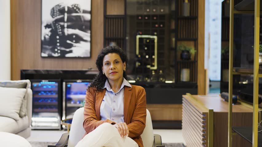 Confident African American businesswoman seated comfortably, exuding professionalism in a stylish living room. Her poised demeanor reflects a blend of elegance and authority in a residential setting