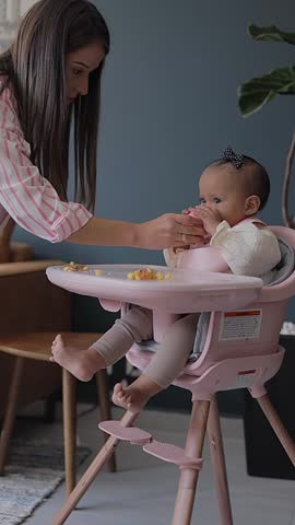 A mother gives her baby water from a glass while she eats while sitting in her chair Royalty-Free Stock Footage #3453357437
