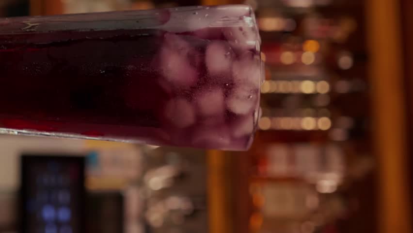 Fresh cocktail in a glass full of ice cubes on a table at a bar background. Professional bartender serve tube into cocktail with ice a mix of syrup or alcohol. vertical Royalty-Free Stock Footage #3453422331
