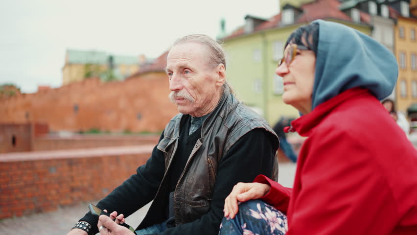 Elderly married couple sit on the parapet, chating and sightsee at Palace Square in Warsaw, Poland, Slow motion, handheld camera
