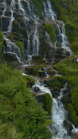 VERTICAL: Green ferns and grass surround waterfall cascading down granite rocks. An ethereal and calming feeling at stunning Brides Veil Falls on picturesque Isle of Skye in northern part of Scotland.