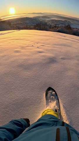 VERTICAL POV: Unrecognizable snowboarder riding powder, carving down the slope with his dog on a sunny morning. Unknown man in ski equipment freeride snowboarding fresh powder snow along with his dog