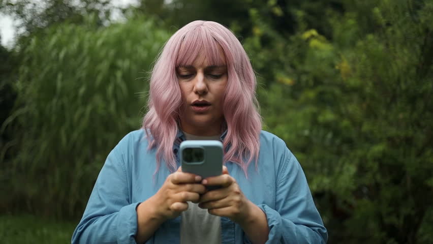 Portrait of nervous unhappy young Caucasian pink hair woman feeling annoyed when getting message on her phone at city street. Annoyed female having problem conflict by smartphone outdoors.   Royalty-Free Stock Footage #3453442543