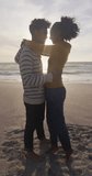 Vertical video of happy biracial couple embracing on sunny beach. healthy, active time beach holiday.